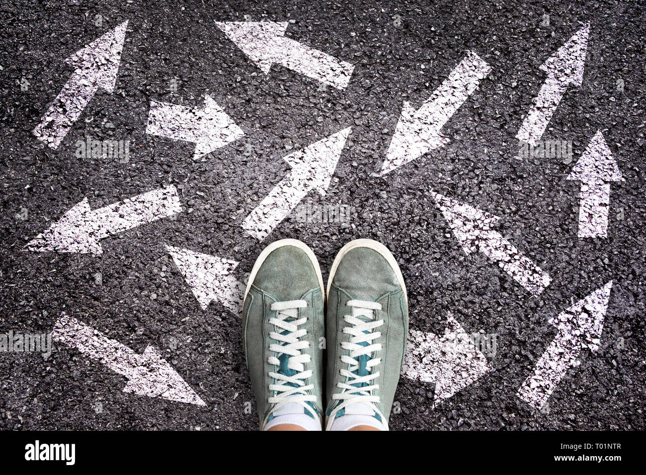 Sneaker scarpe e le frecce che puntano in direzioni differenti sulla massa di asfalto, concetto di scelta Foto Stock