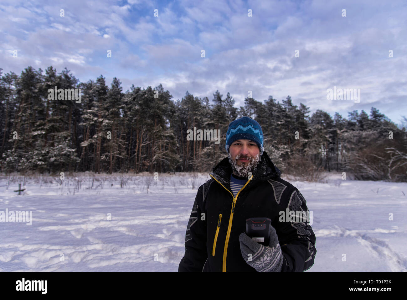 Bonario uomo barbuto con una barba nevoso, leggero sorriso e il GPS Navigator è in piedi sul bordo di una foresta taiga Foto Stock