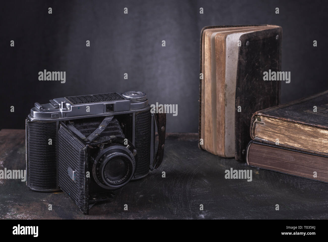 Una telecamera storico con tre vecchi libri su uno sfondo nero in una sala dalla parete. Foto Stock