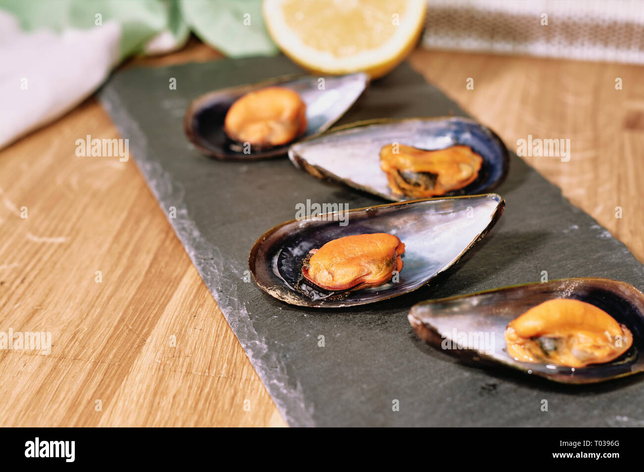 Le cozze al vapore sulla tavola di ardesia e tavolo in legno Foto Stock