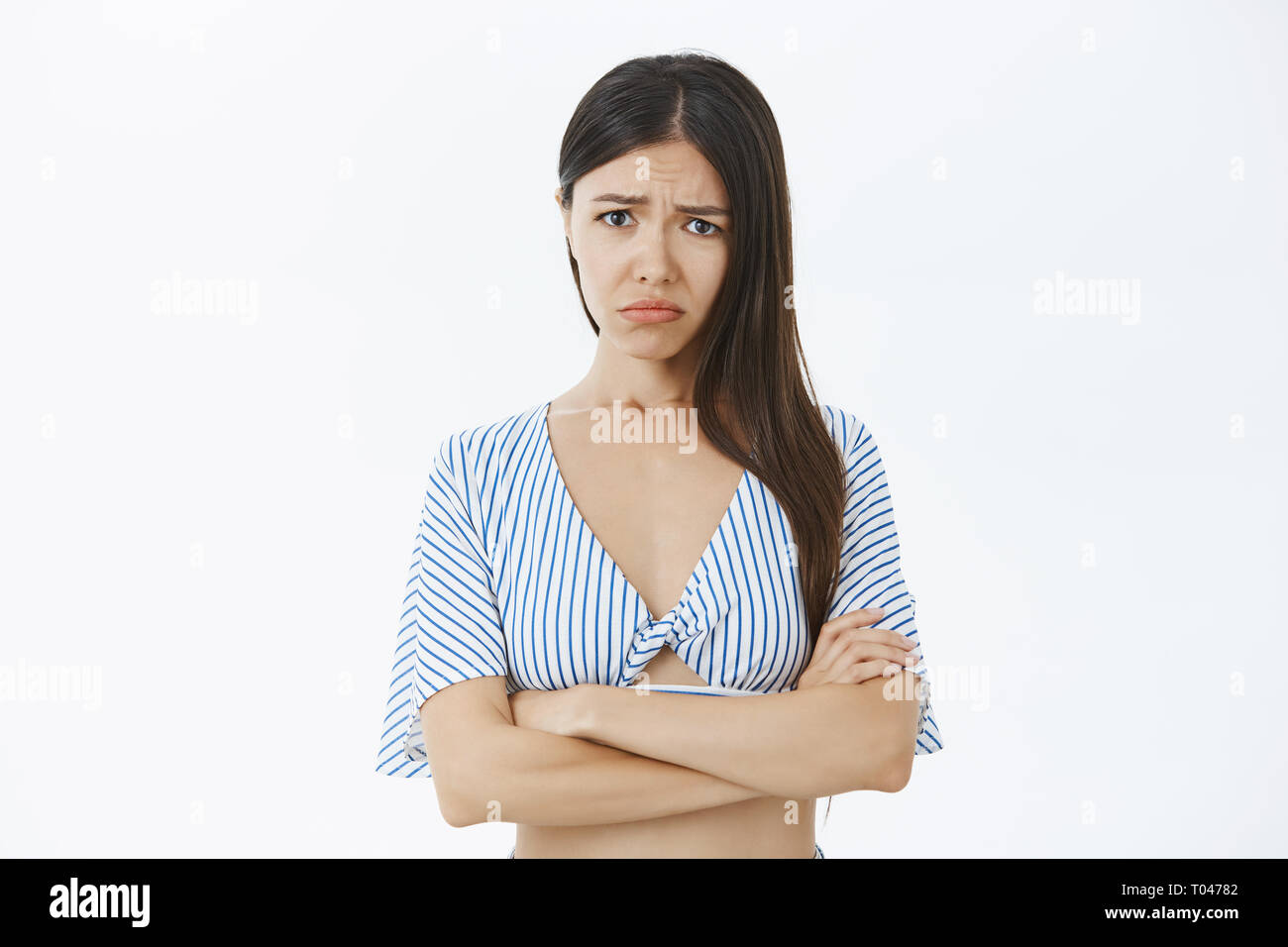 Silly whining ragazza con lunghi capelli scuri esercitano le labbra e accigliata lamenta sulla vita sleale sentimenti di gelosia e invidia tenendo le mani incrociate Foto Stock