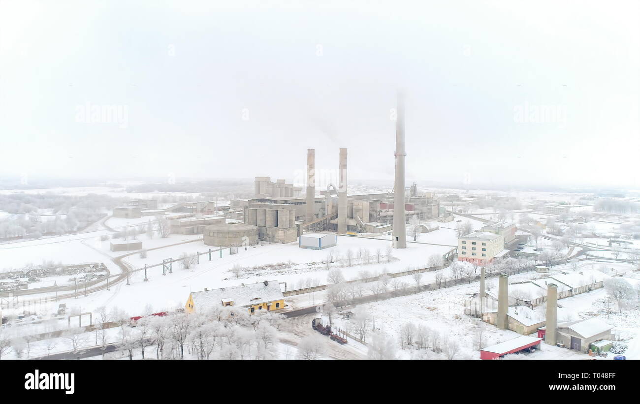 Vista aerea della fabbrica nevoso in Kunda estonia con molto bianco neve spessa su terra alta torre tubazione della fabbrica su una stagione invernale Foto Stock