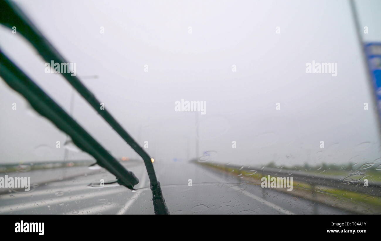 Heavy Rain versando al di fuori mentre sulla strada come si vede sul cruscotto Auto della fotocamera e i tergicristalli sulla parte anteriore Foto Stock