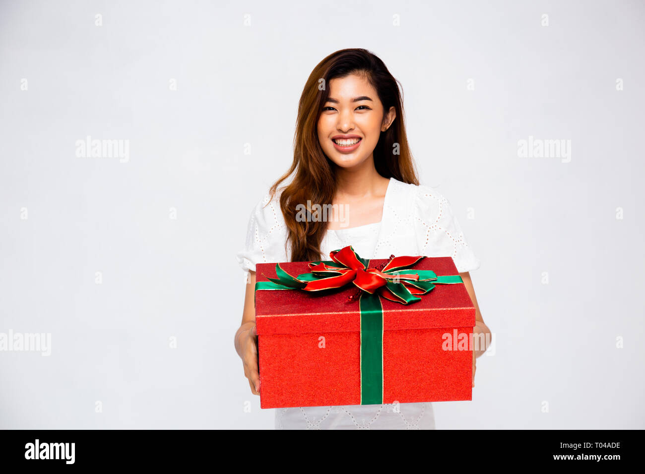 Bella femmina asiatica sorridente e dando grande confezione regalo per fotocamera mentre in piedi su sfondo grigio Foto Stock