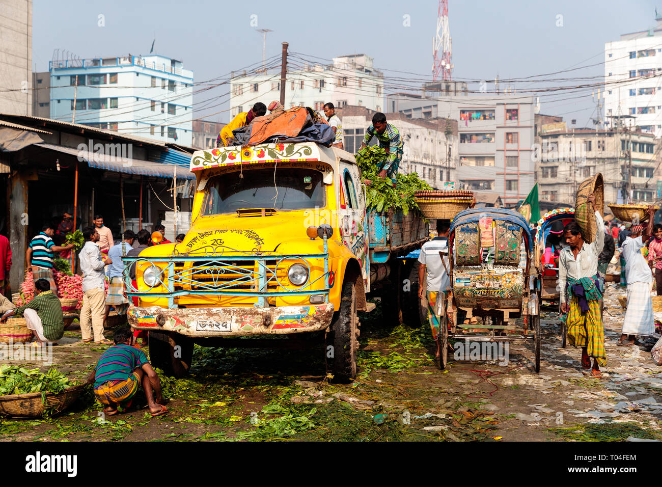 Coloratissimo mercato della frutta con van e risciò e persone che trasportano merci nelle strade di Dacca in Bangladesh Foto Stock