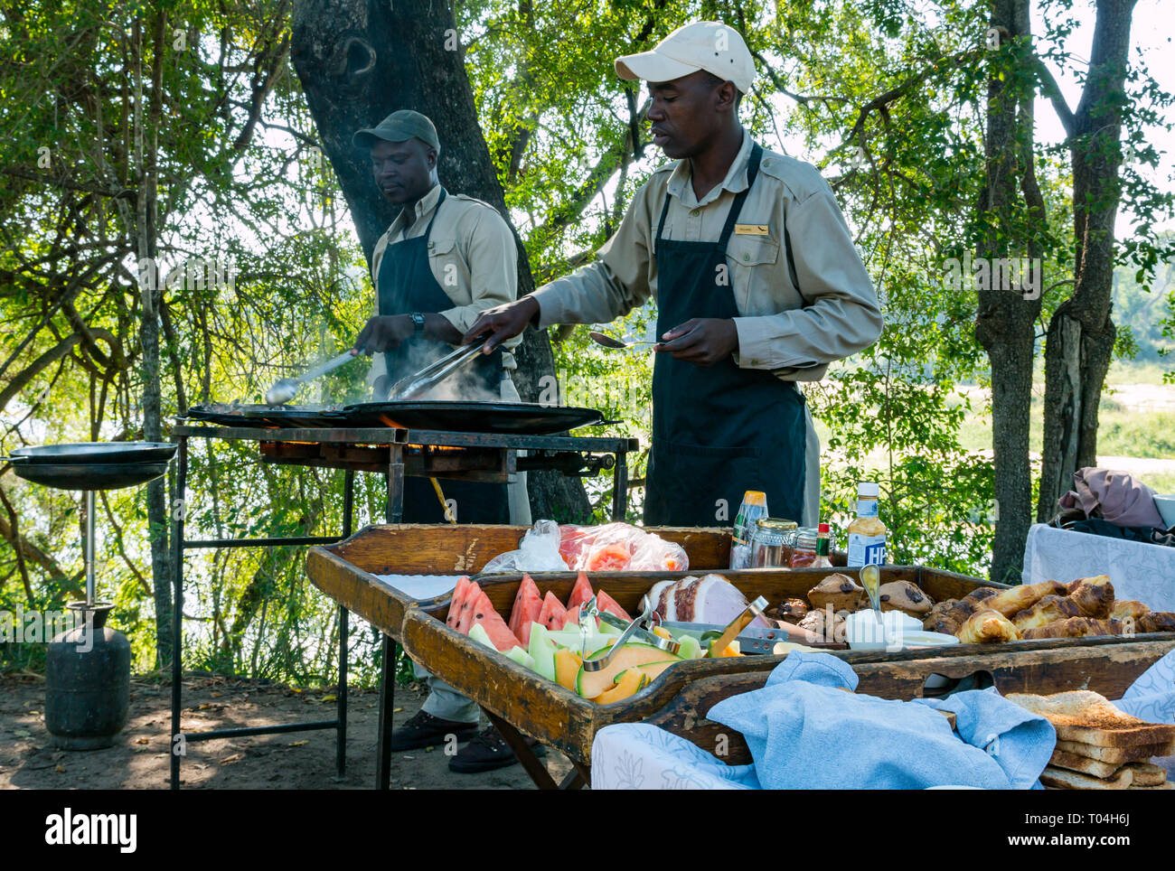 Il personale nero cooking per colazione sul grill esterno per Safari gli ospiti di Sabi Sands Game Reserve, Sud Africa Foto Stock