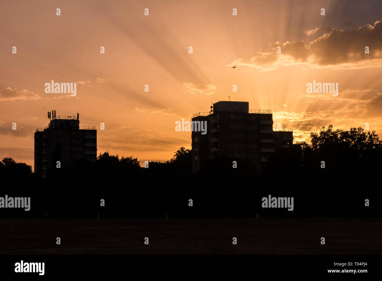 I raggi di luce da un tramonto urbano con blocchi a torre in primo piano e un piano in arrivo a terra all'Aeroporto di Londra Heathrow Foto Stock