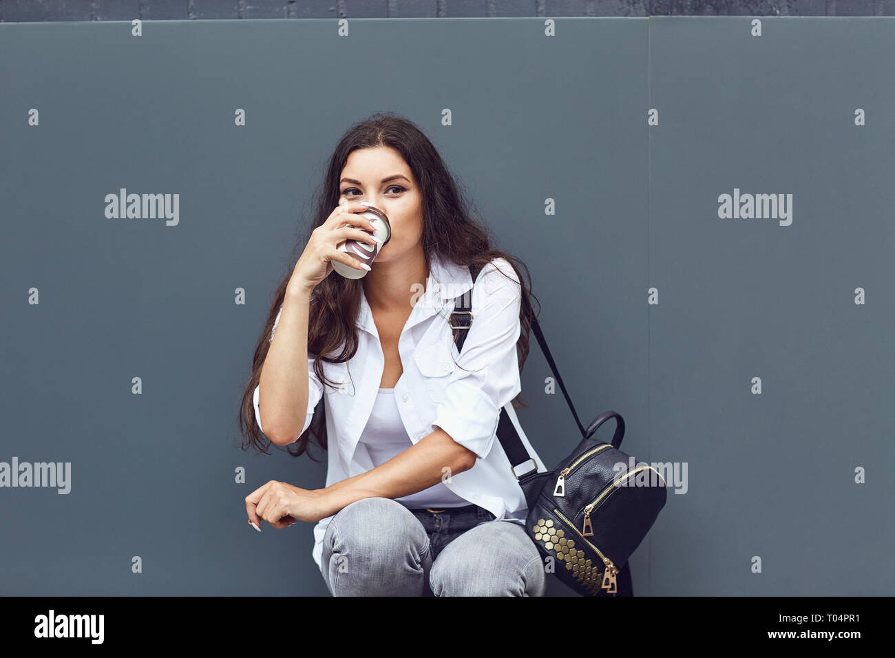 Una bruna ragazza con una tazza da caffè sorride all'aperto. Foto Stock