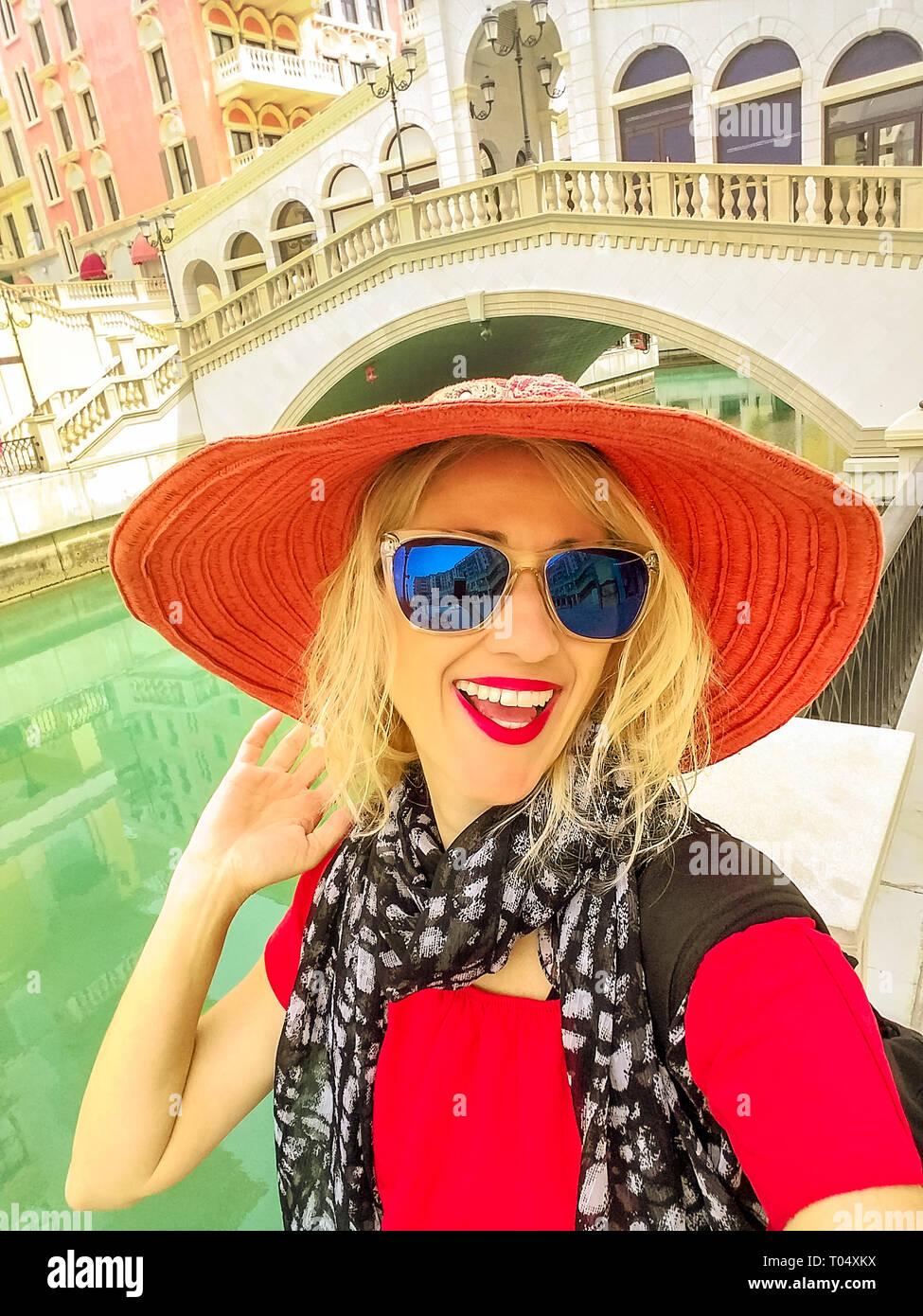 Donna felice selfie vicino al famoso ponte di Venezia, uno stile veneziano Waterfront village. Caucasian turista gode Qanat Quartier in Pearl-Qatar, icona Foto Stock