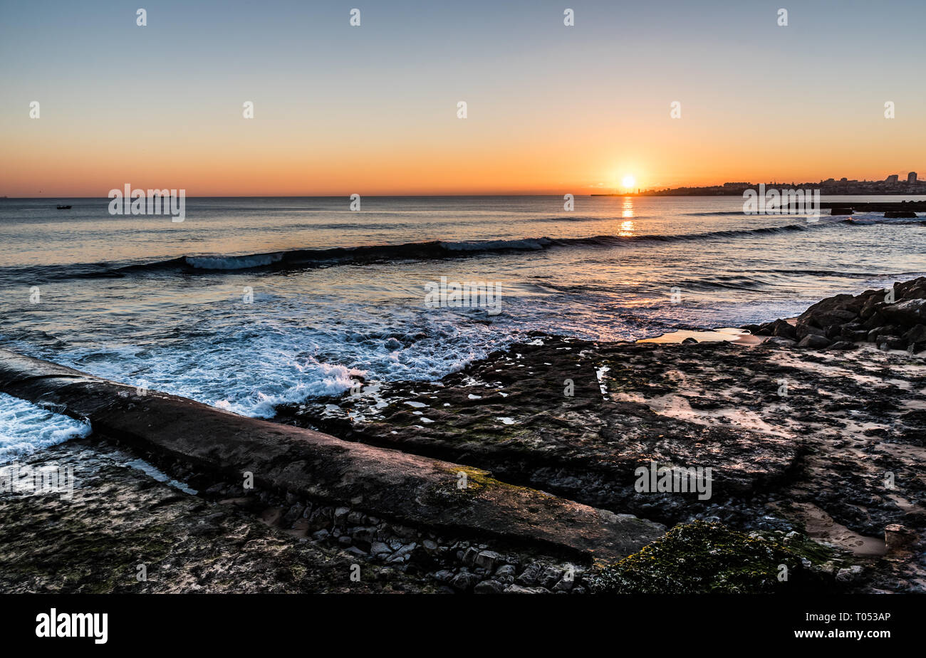 Spiaggia rocciosa con piccole onde e un colorato tramonto all'Oceano Atlantico a Estoril, Portogallo Foto Stock