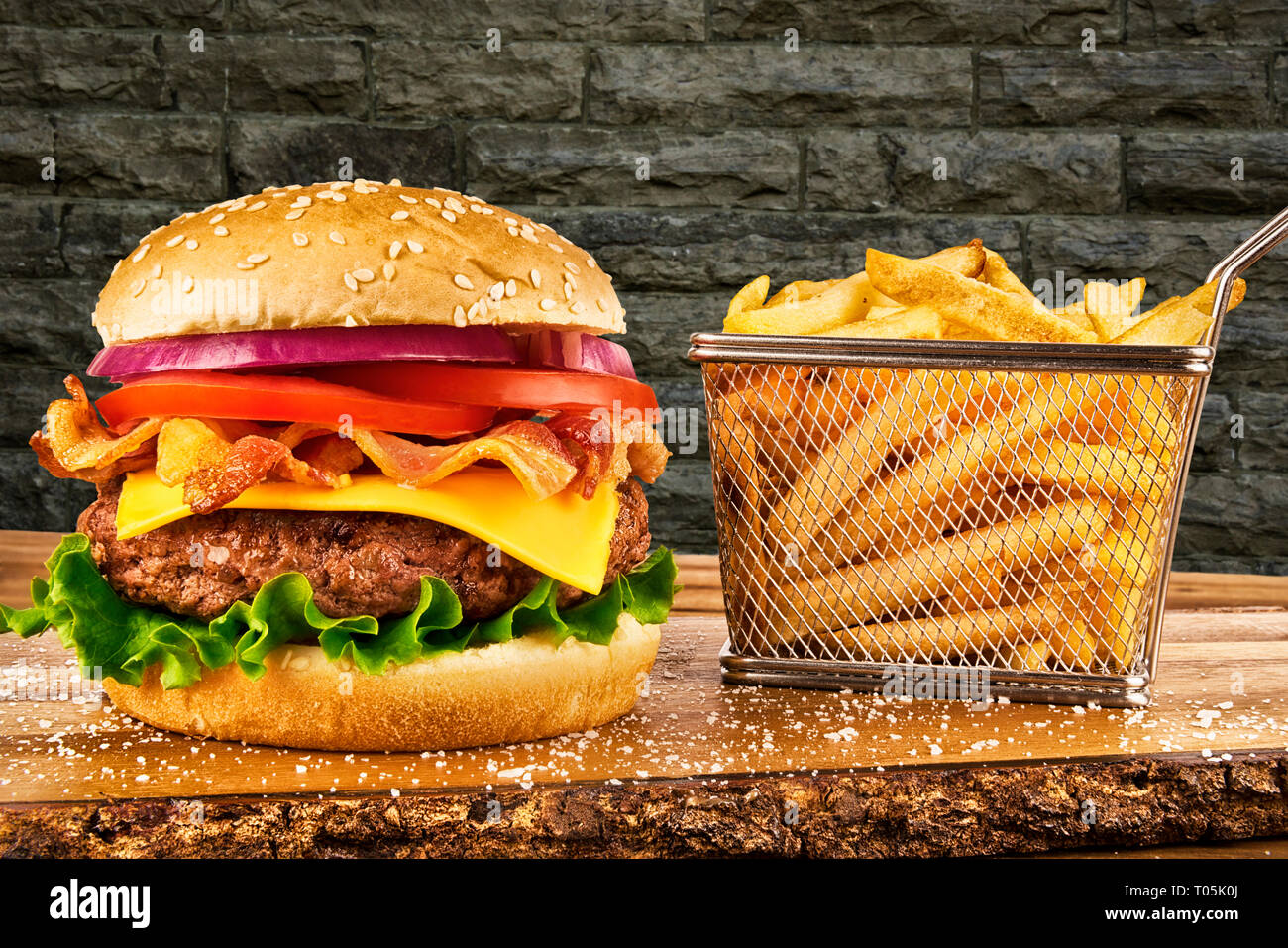 Cheeseburger con pancetta e un cestino di patatine fritte. Muro di mattoni in background. Copia dello spazio per il tuo testo. Foto Stock