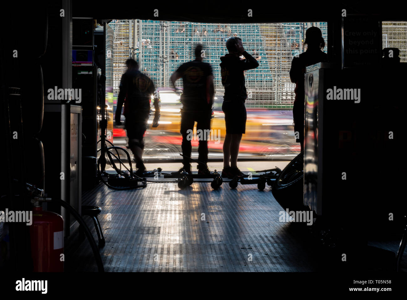 Quattro pit crew, in silhouette, guardando le vetture passano da sulla pit lane Foto Stock