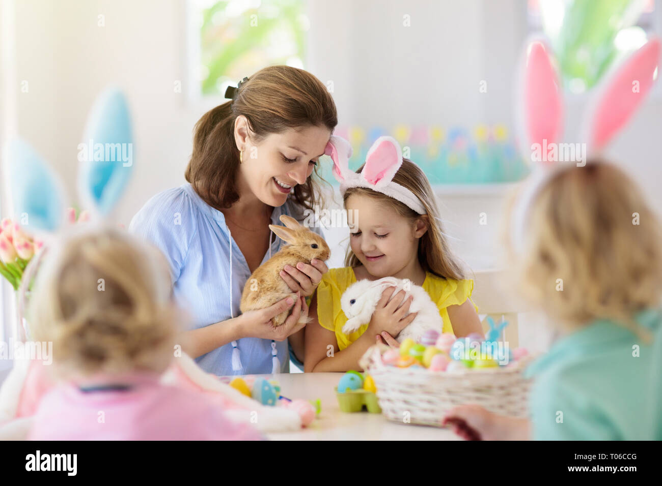 Madre e bambini con pet colore di coniglio uova di Pasqua. Mom, bambina e ragazzo con orecchie di coniglietto di tintura e pittura per uovo di Pasqua Caccia in bianco stanza soleggiata Foto Stock