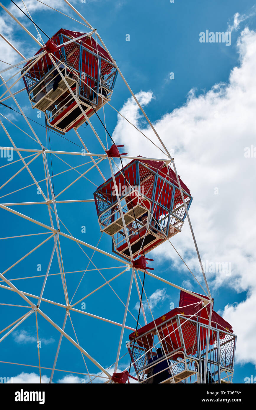 Close up di tre rossi ruota panoramica Ferris capsule contro una vibrante cielo blu e nuvole bianche. Foto Stock