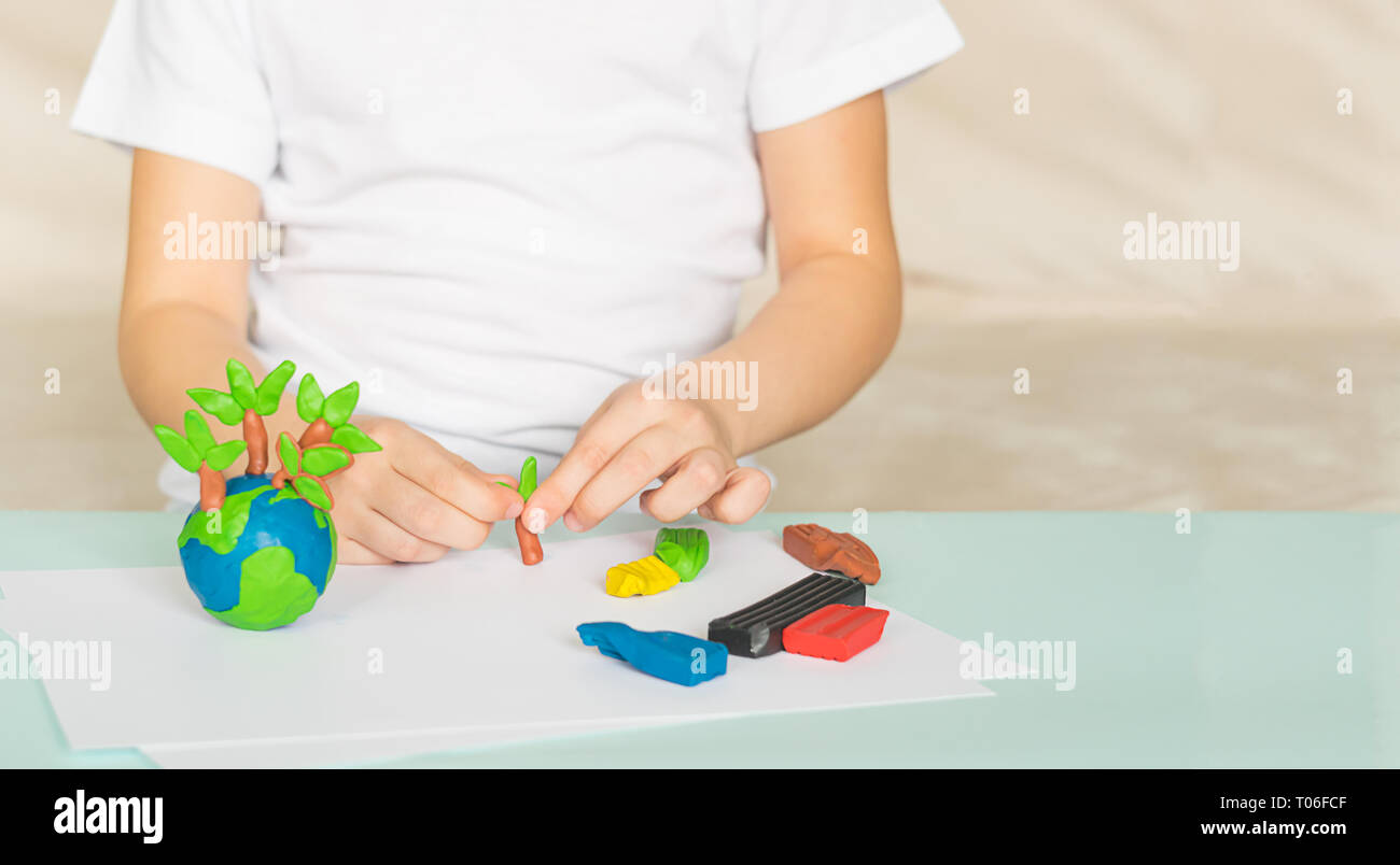 Il fanciullo scolpisce da plastilina il globo e alberi. La posizione del pianeta in bambini di palme. Concetto di ecologia. Foto Stock