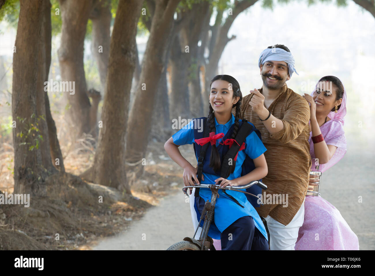 Felice coppia rurale insieme con la loro figlia equitazione sulla bicicletta nel villaggio. Foto Stock