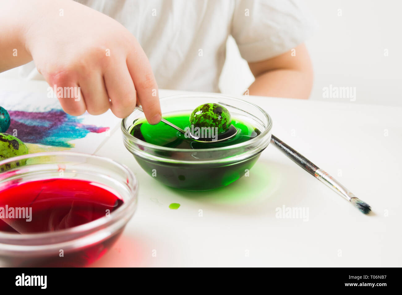 Bambino la mano che regge il cucchiaio con uovo verde, bambino dipinto uova di quaglia per Pasqua sul tavolo bianco Foto Stock