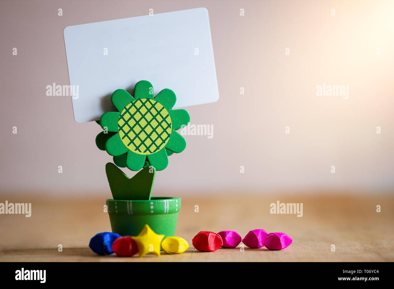 Clip di supporto supporto carta verde a forma di girasole e multicolore di stelle di carta su un tavolo di legno. In plastica bianca scheda vuota nella luce del sole di mattina. Foto Stock