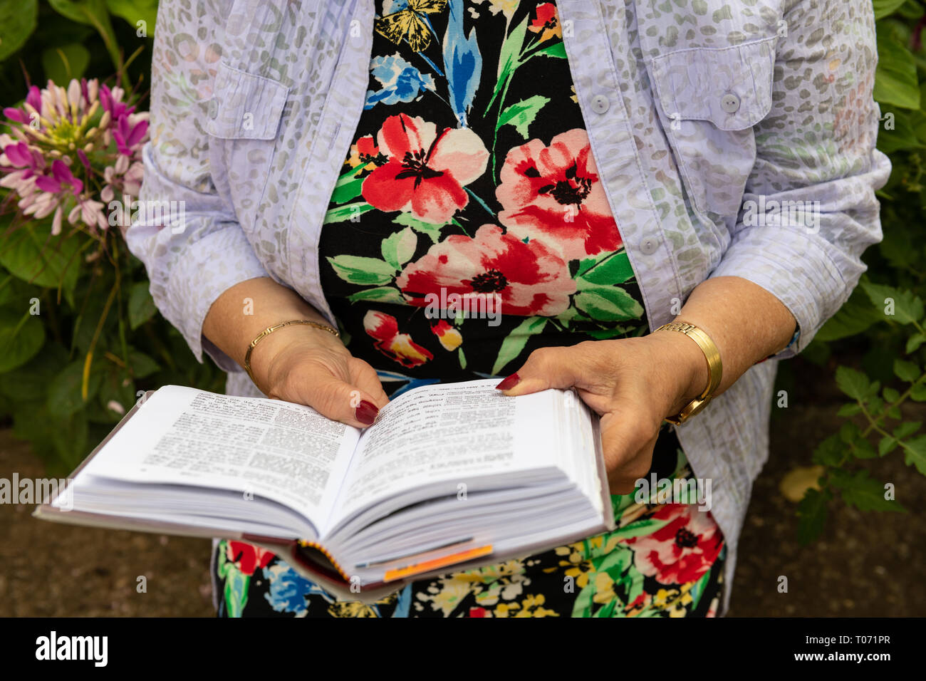 I vecchi donna ebrea indossare gioielli legge il suo libro di preghiere nel giardino sul retro. Prenota e le mani di close-up. Foto Stock