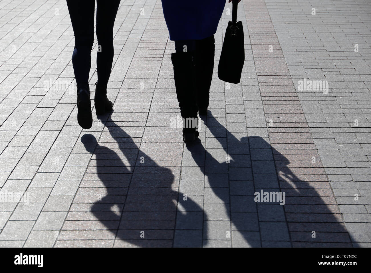 Due donne a camminare per la strada, nero sagome e ombre sul marciapiede. Gambe Slim in stivali, concetto di moda femminile, l'amicizia, la vita drammatica Foto Stock