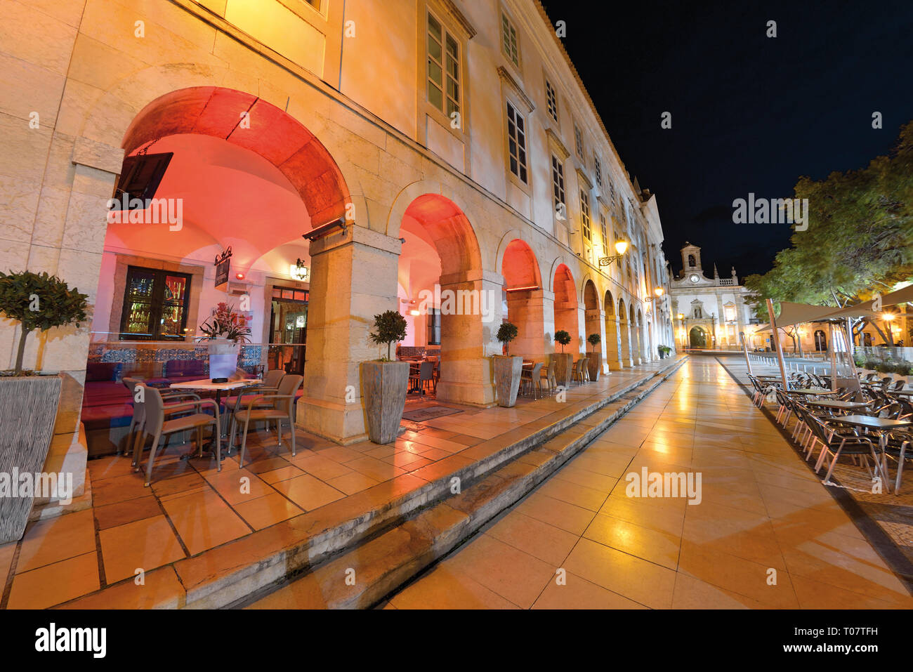 Orologio notturno illuminato edificio con archi e piazza con pavimentazione in ciottoli Foto Stock