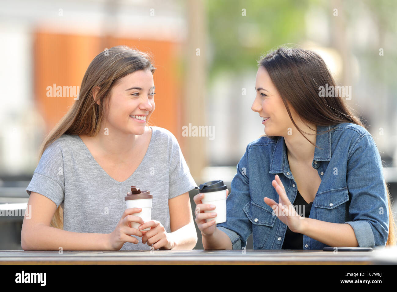 Due amici felice di parlare e di bere seduti in un parco Foto Stock