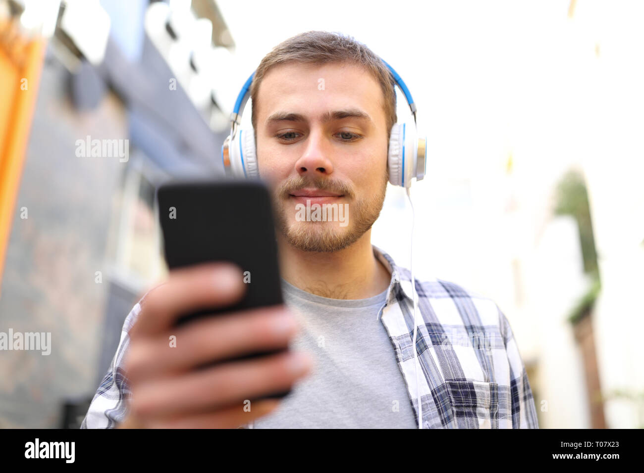 Vista frontale di un serio uomo ascoltare musica controllo smart phone a piedi in strada Foto Stock