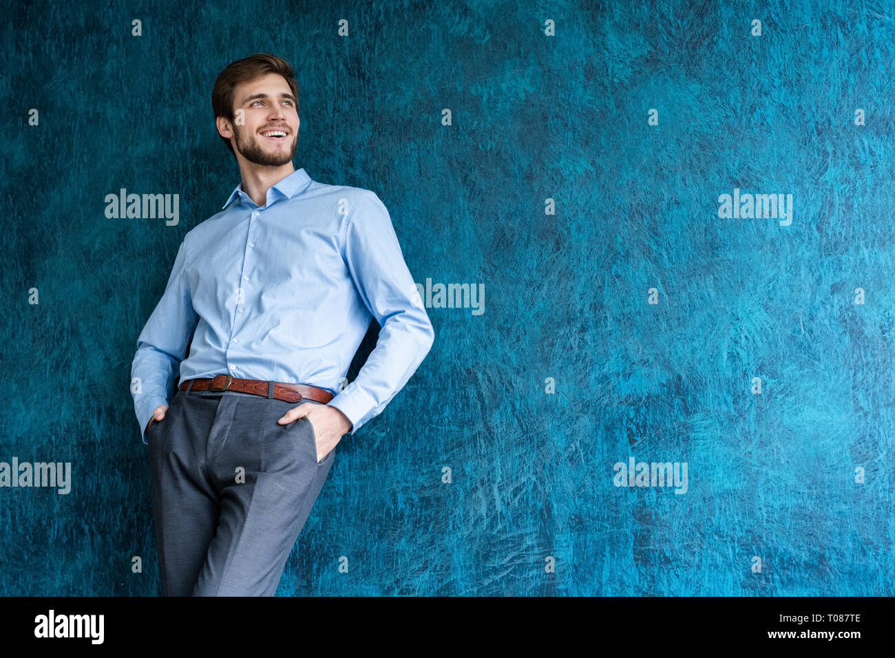 Ritratto di bel giovane uomo in piedi contro la parete blu con copia spazio. Foto Stock