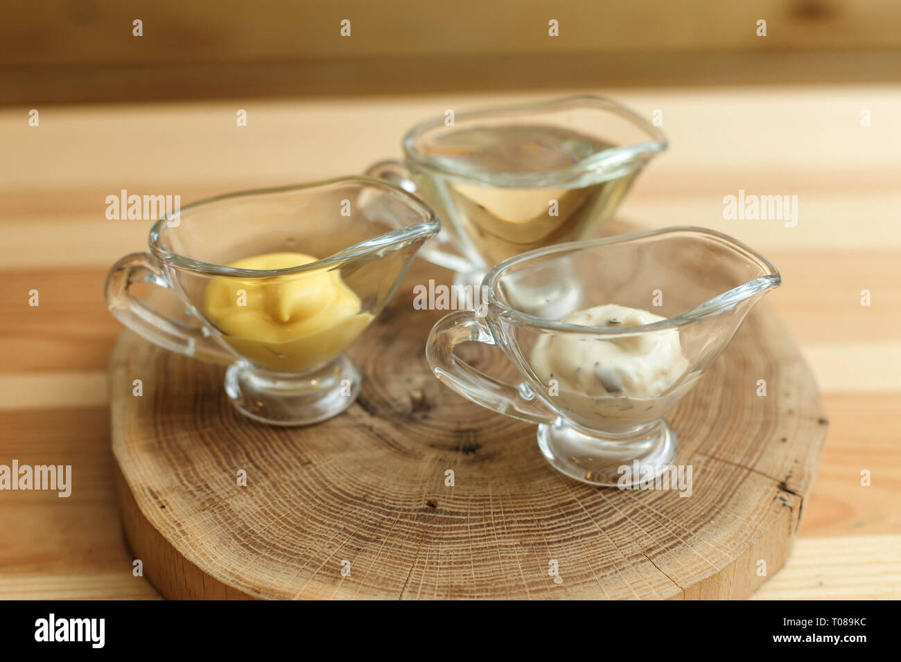 Set di tre sauceboats trasparente con diverse salse sul piatto di legno. Foto Stock