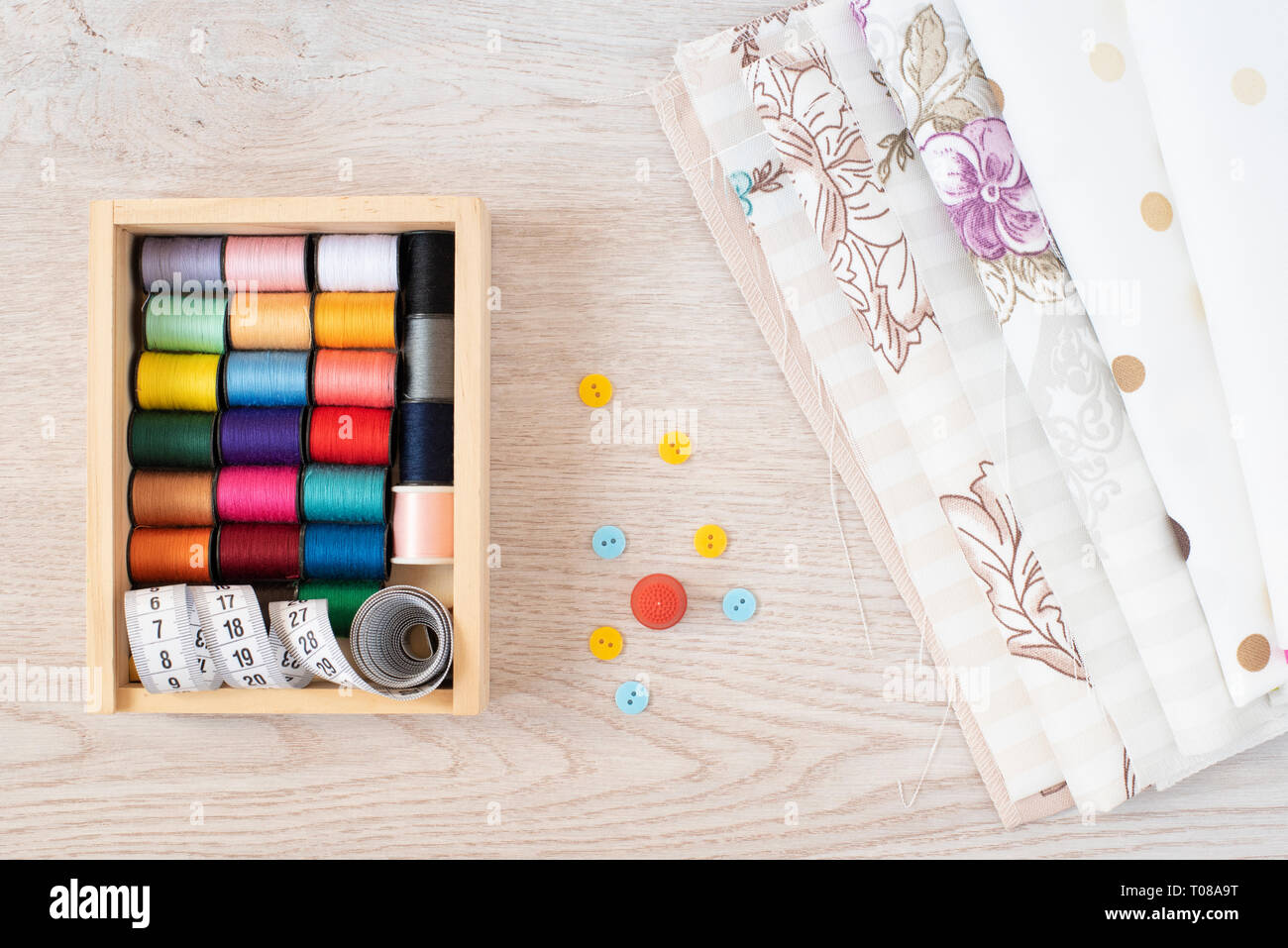 Composizione con fili di cucitura, tessuti e accessori su sfondo di legno, vista dall'alto Foto Stock