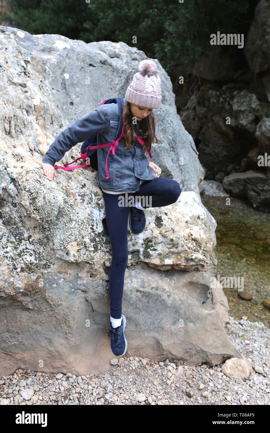 Ragazza giovane e carina con beanie e zaino arrampicata su roccia una escursione Foto Stock