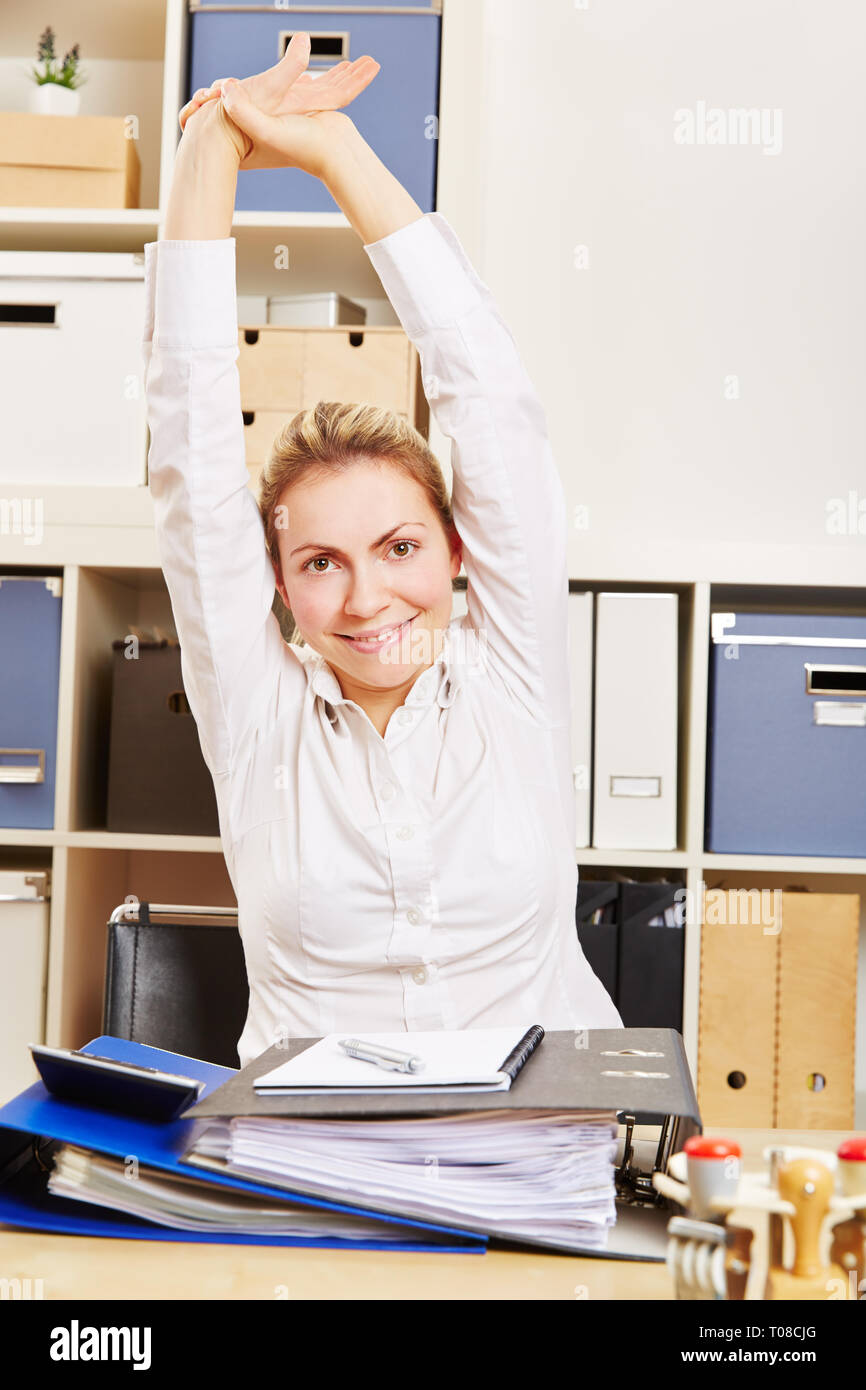 Giovane donna sorridente si allunga le braccia in ufficio come esercizio indietro Foto Stock