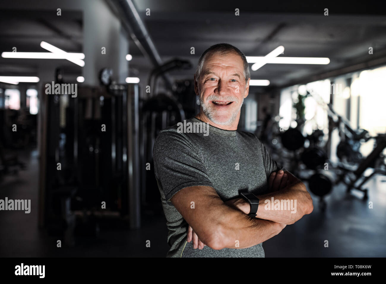 Un allegro senior man standing in palestra, con le braccia incrociate. Foto Stock