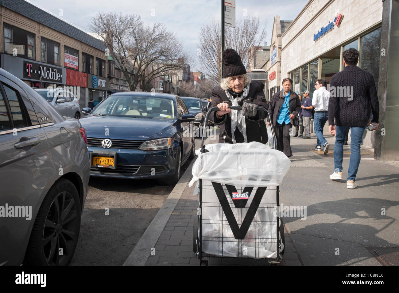 Una donna più anziana in un cappello di maglia spingendo un carrello su 82st in Jackson Heights, Queens, NYC vicino al #7 treno . Foto Stock