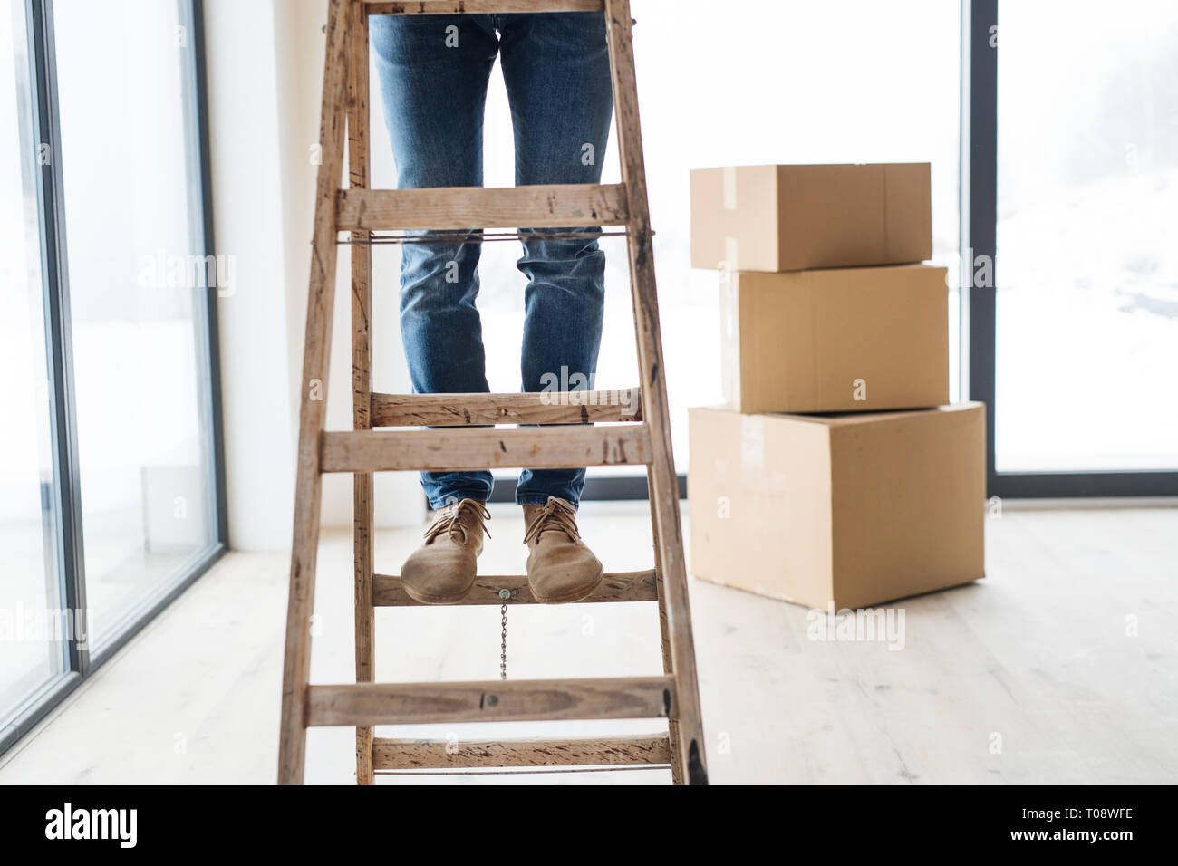 Una sezione mediana dell'uomo con le scatole di cartone in piedi su una scaletta, arredamento casa nuova. Foto Stock