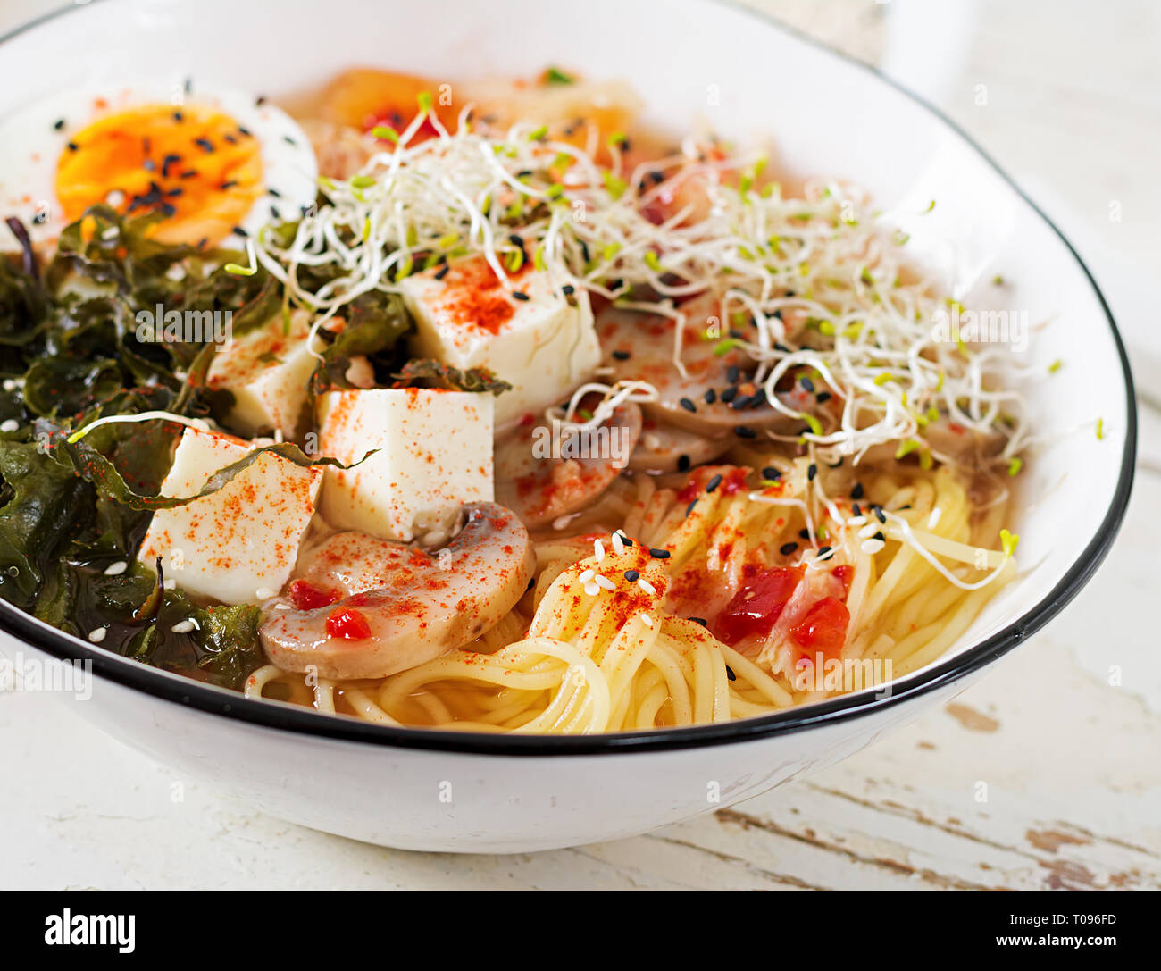 Miso Ramen noodle asiatici con cavolo kimchi, alghe, uovo, funghi e formaggio tofu in vaso bianco sul tavolo di legno. Cucina Coreana. Foto Stock