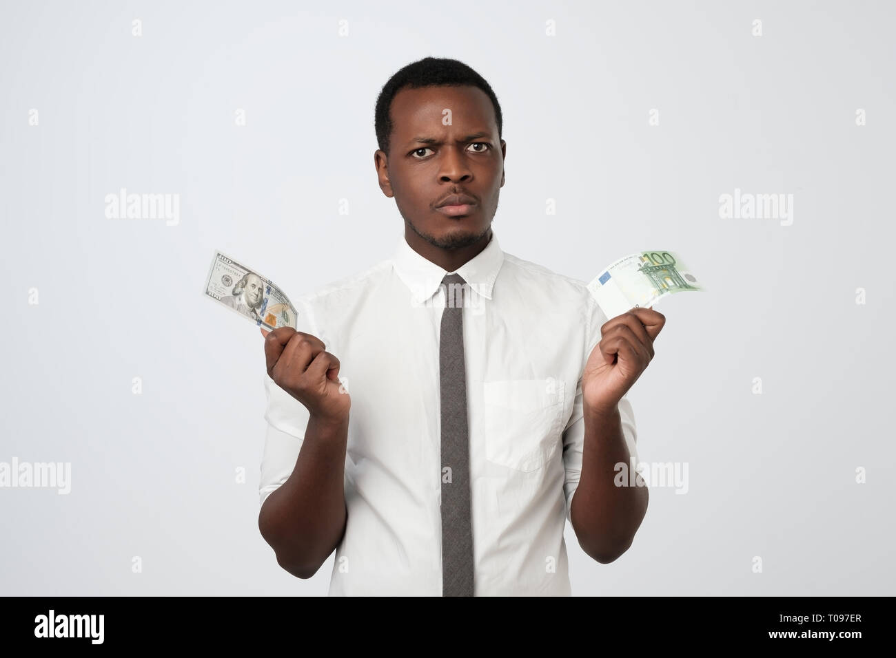 Giovani attraenti uomo africano azienda usa la valuta e la valuta euro di decidere quale scegliere. Foto Stock