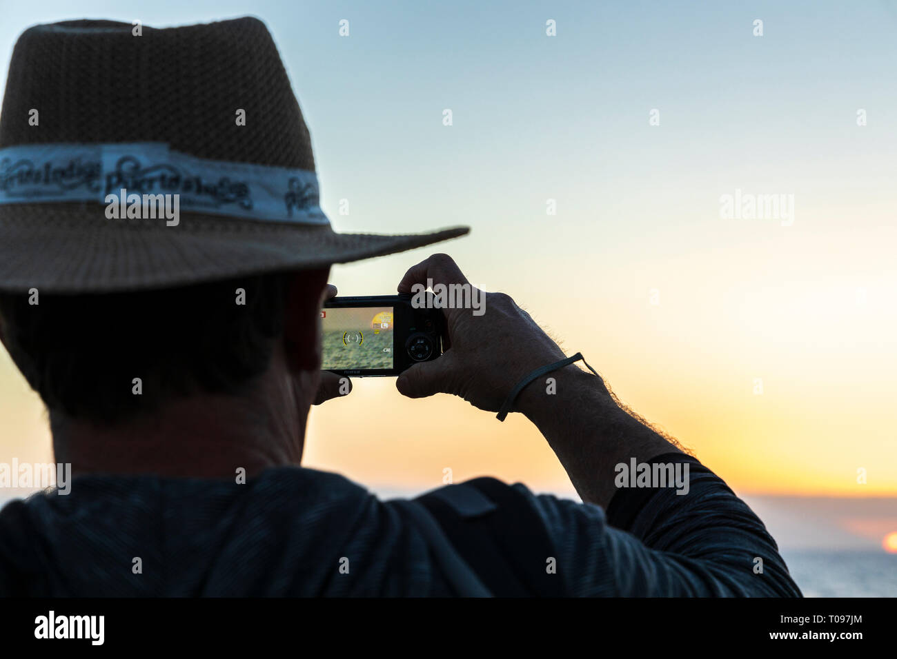 L'uomo con il cappello di paglia per fotografare il tramonto visto da Playa de la Arena sulla costa occidentale di Tenerife, Isole Canarie, Spagna Foto Stock