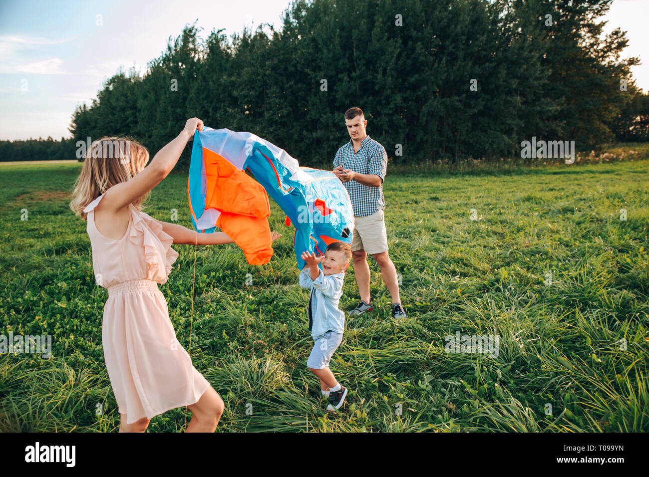 La famiglia felice padre, madre e figlio figlio lanciare un aquilone sulla natura al tramonto Foto Stock