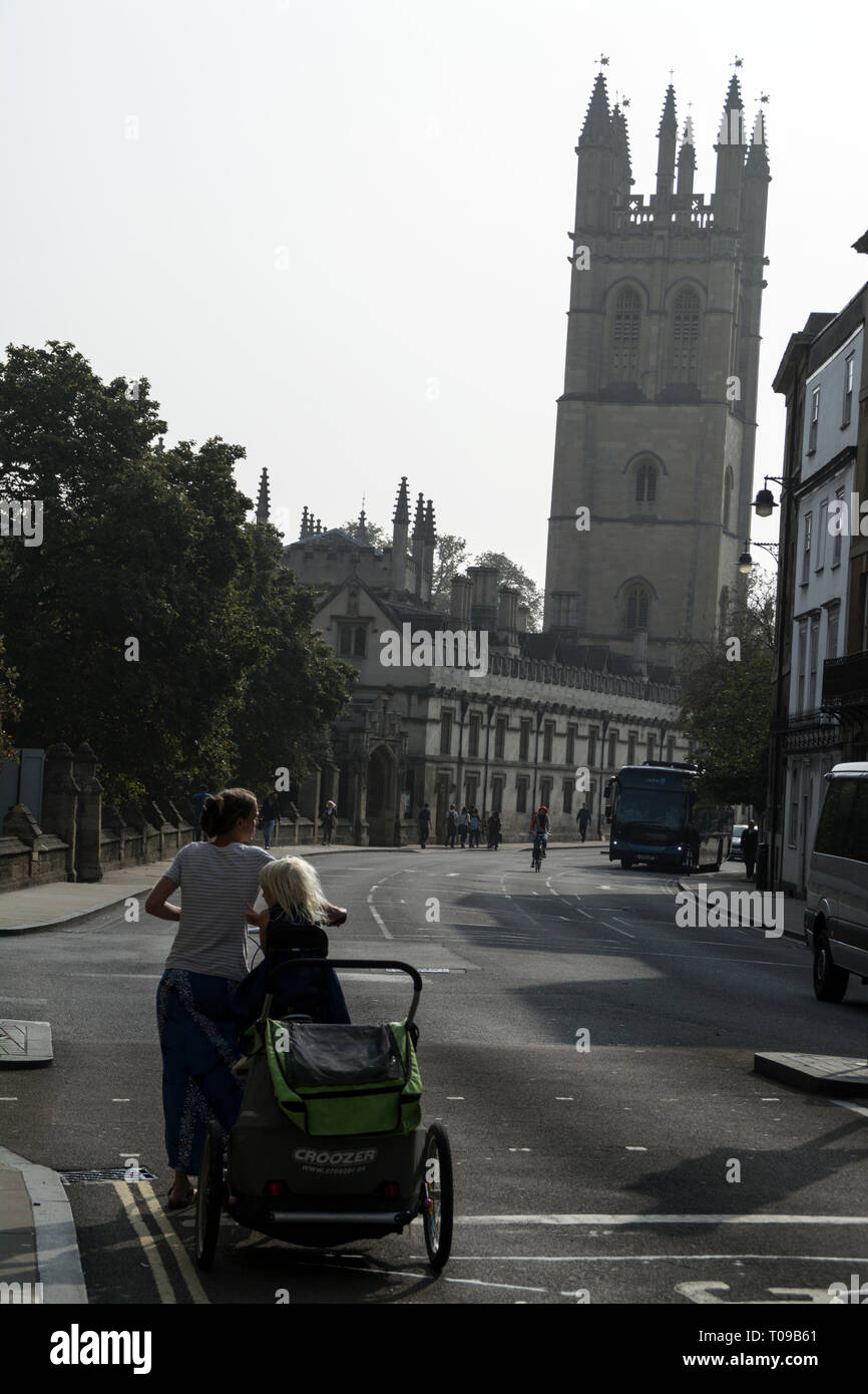 Un ciclista con un bambino di buggy fissata rivolta Magdalen Tower in High Street, Oxford,Oxfordshire, Gran Bretagna Foto Stock