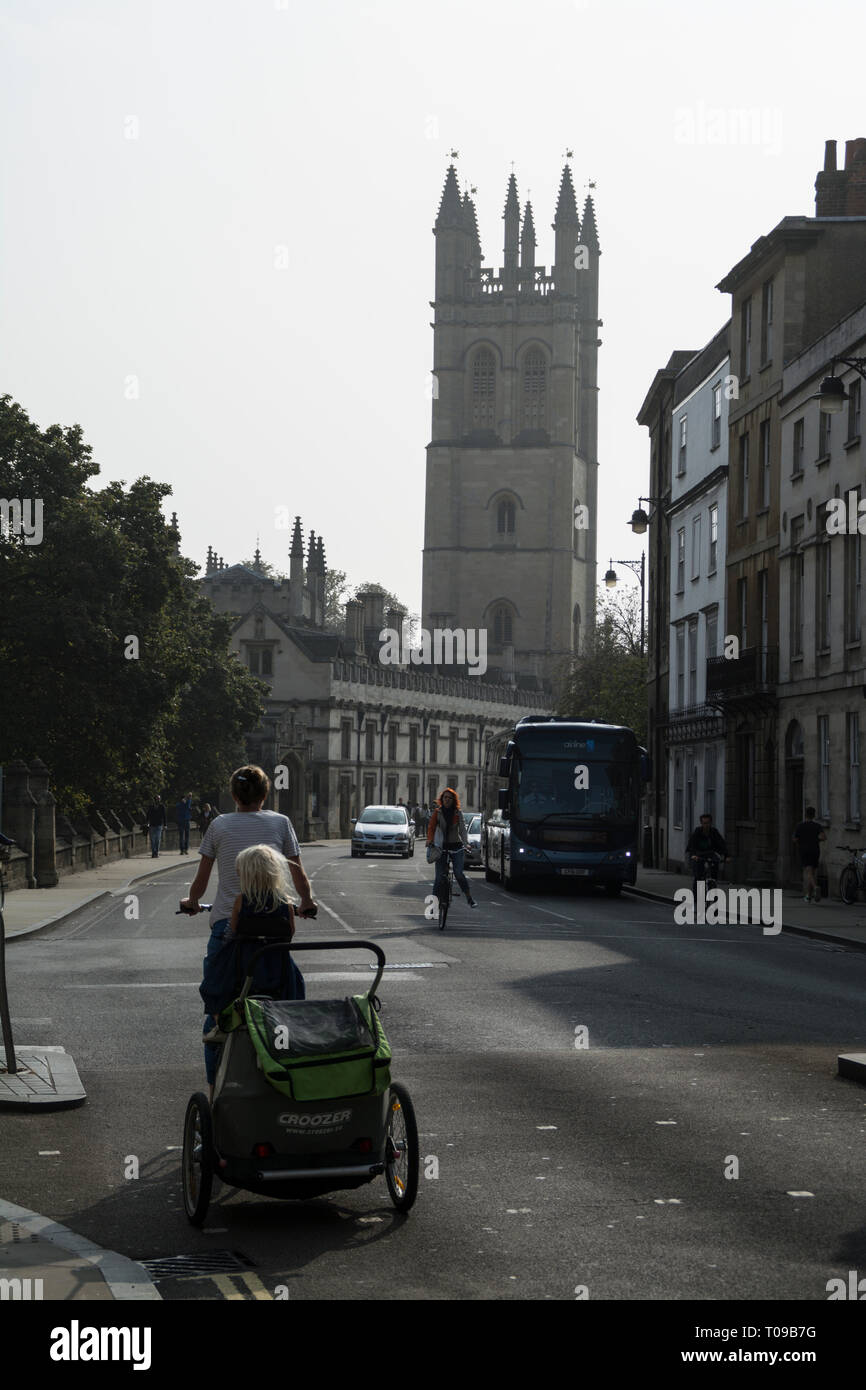 Un ciclista con un bambino di buggy fissata rivolta Magdalen Tower in High Street, Oxford,Oxfordshire, Gran Bretagna Foto Stock