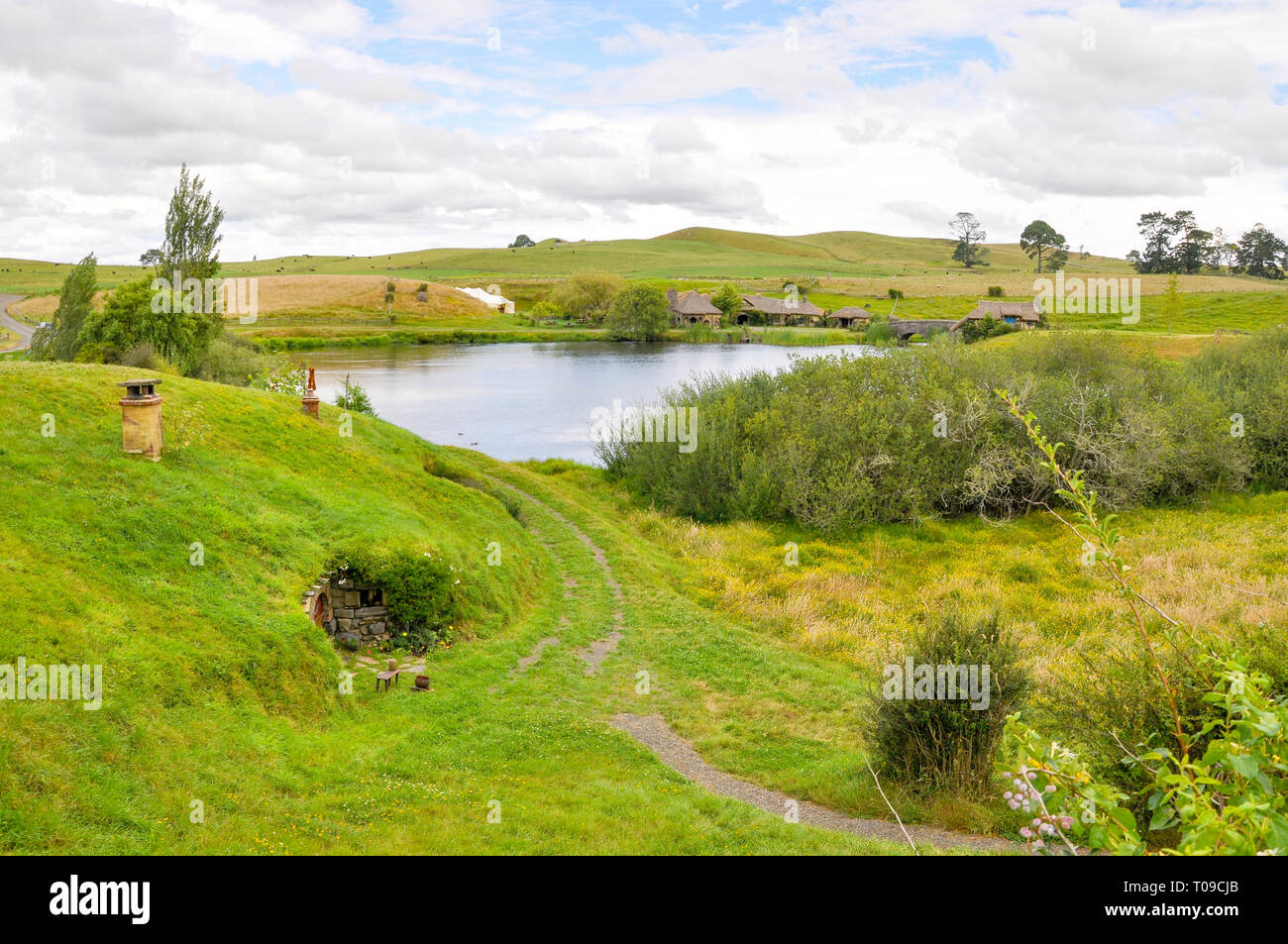Hobbiton movie set nella regione di Waikato della Nuova Zelanda Isola del nord. Colline della Shire con foro Hobbit lago mill, bridge, Green Dragon Inn. Foto Stock