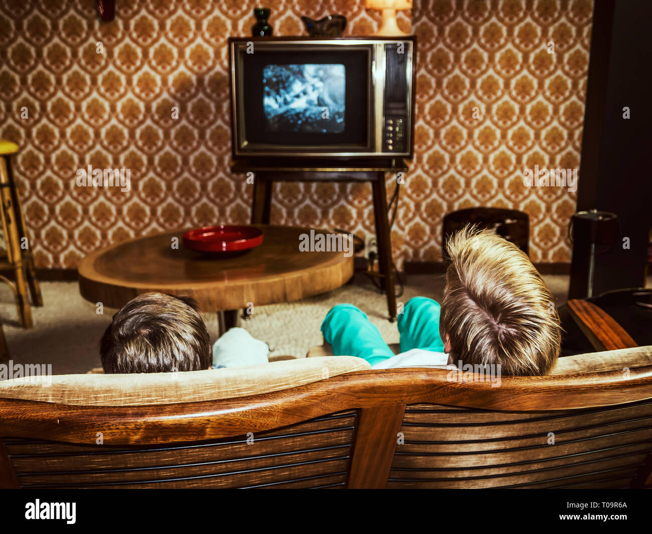 Due ragazzi guardano la televisione a casa in stile anni '50, inquadratura da dietro Foto Stock