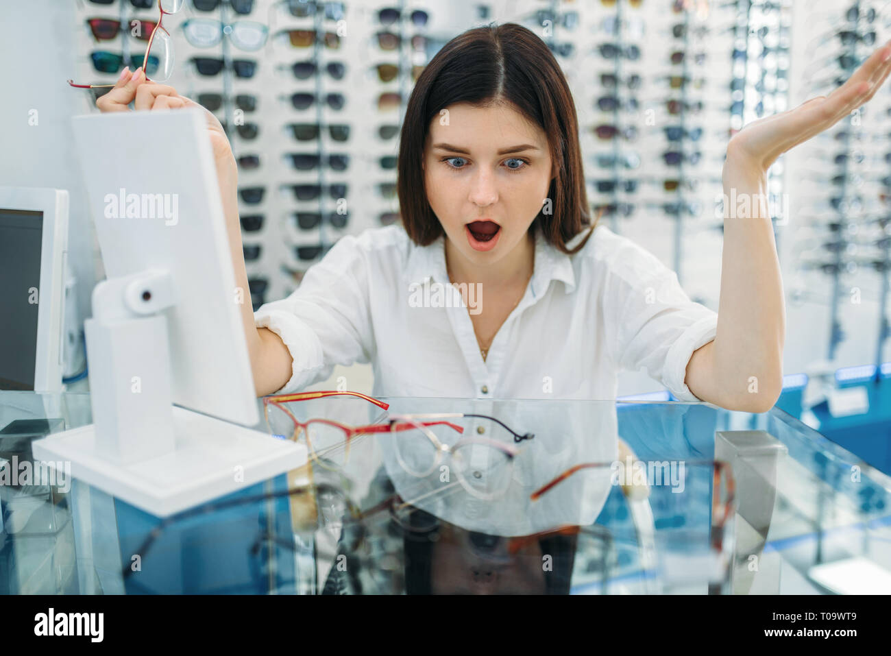 Acquirente femmina sorpreso dall'effetto di occhiali, ottica store, vetrina con occhiali sullo sfondo. Eyecare professionale in occhiali concetto di shop Foto Stock