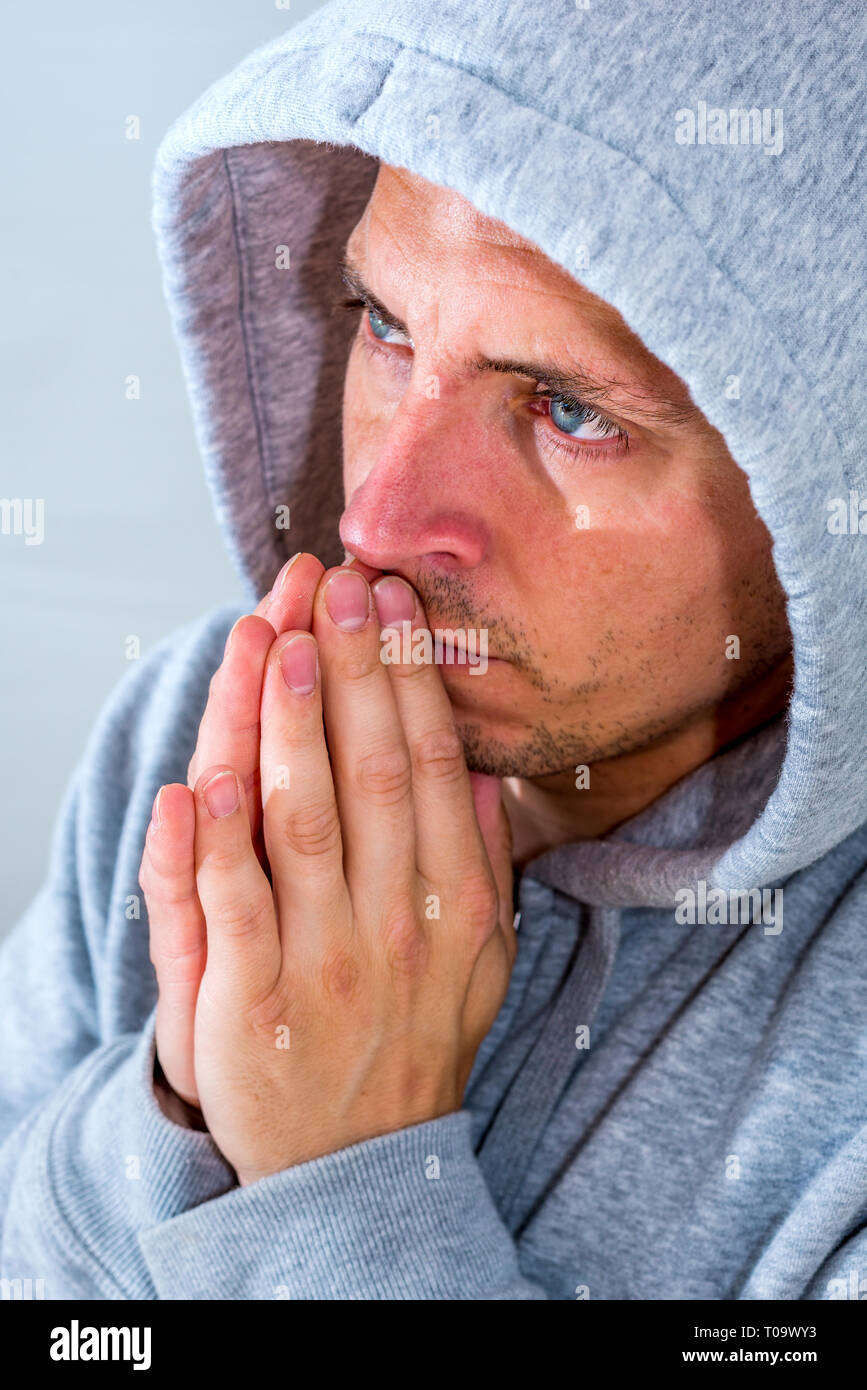 Uomo in camicia con cappuccio pregando e fissando Foto Stock