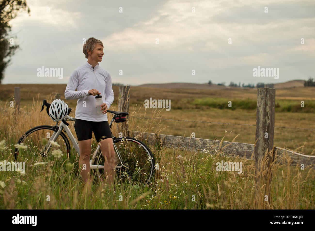 Sorridente donna matura prendendo una pausa dal bike per ammirare un campo rurale. Foto Stock