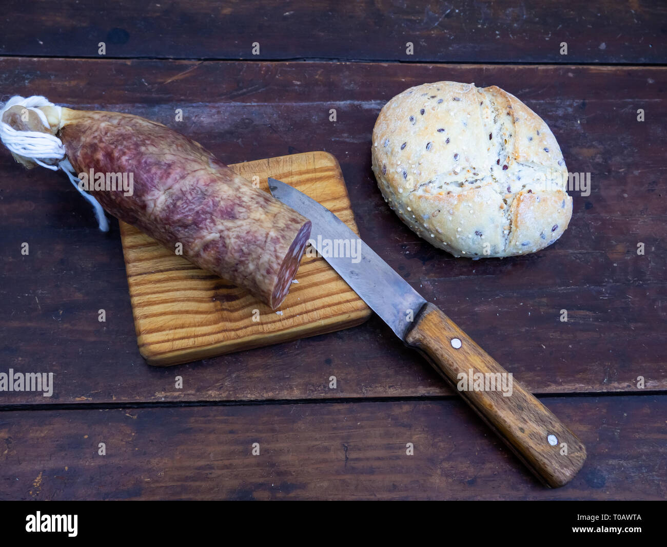Un maiale iberico insaccato su una vecchia tavola di legno con un coltello di antiquariato e una focaccia di spagnolo rustico pane di sementi Foto Stock