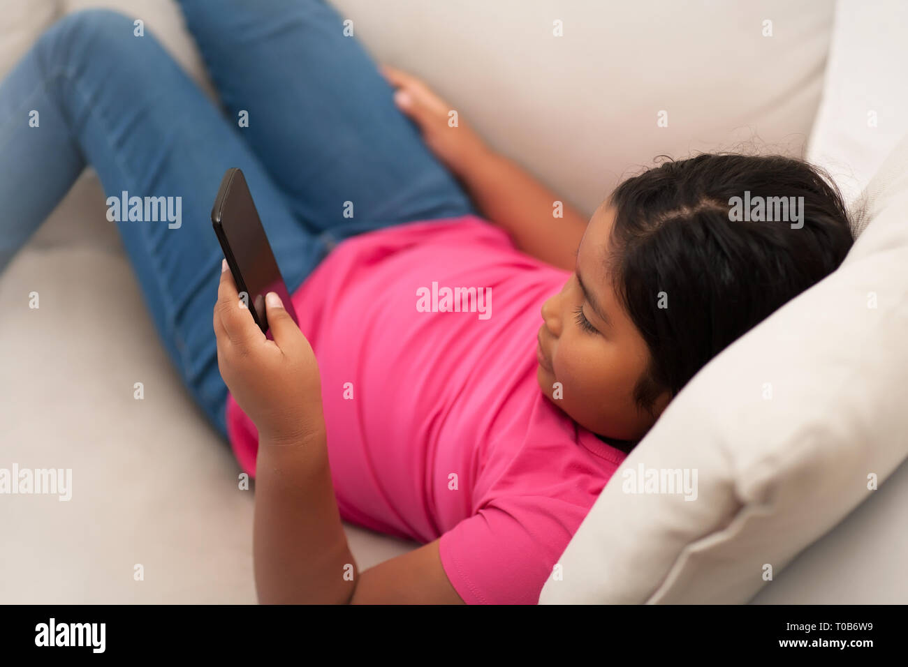 Giovane ragazza seduta con le gambe stese su un lettino usando un telefono a testo o visualizzare i contenuti online senza supervisione. Foto Stock