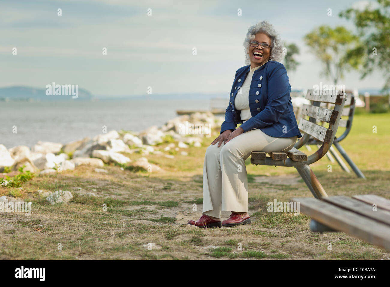 Ritratto di un sorridente senior donna seduta su una panchina nel parco. Foto Stock