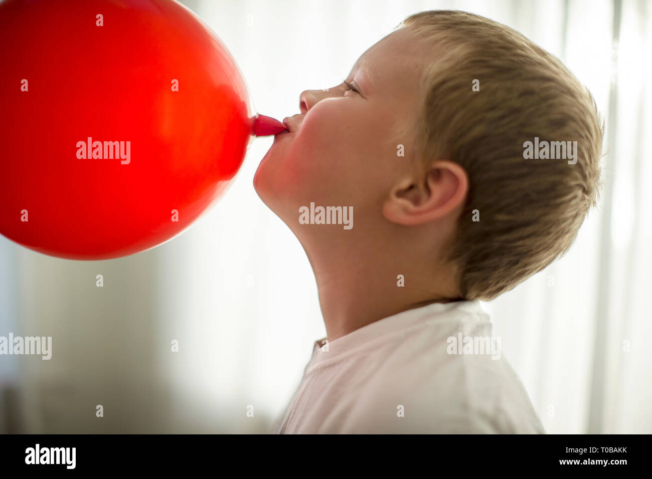 Felice ragazzo avendo divertimento che soffia su un palloncino rosso. Foto Stock